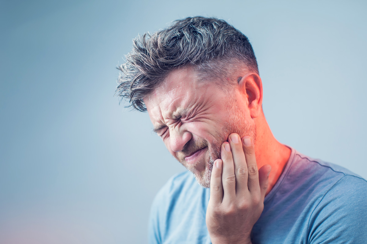 A man in a blue shirt touching his jaw in pain in El Paso.