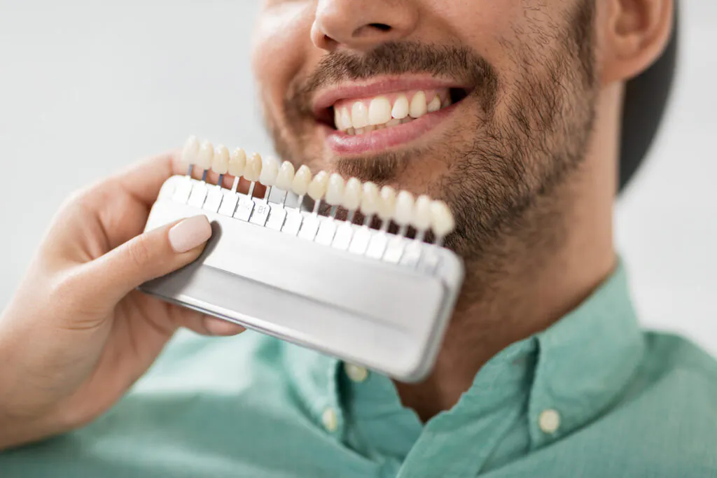 A person holding up a chart of different teeth next to a smiling man.